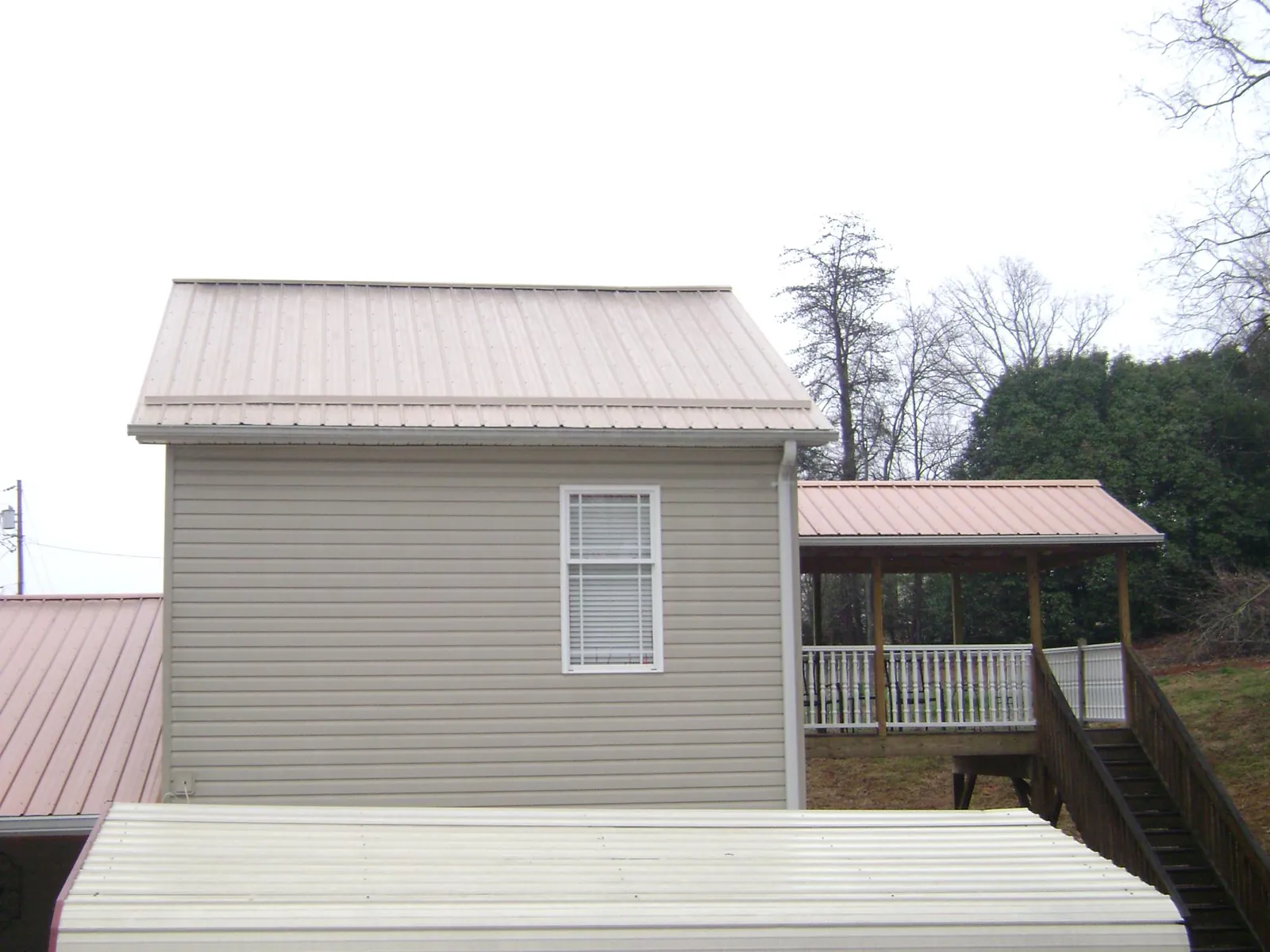 Tan metal roofs on a two story addition and attached porch, from a Roof Replacement job in Milan